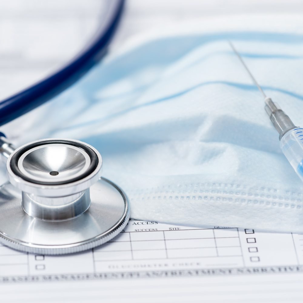 stethoscope-with-injection-protective-mask-lying-over-medical-chart-SBI-300904603